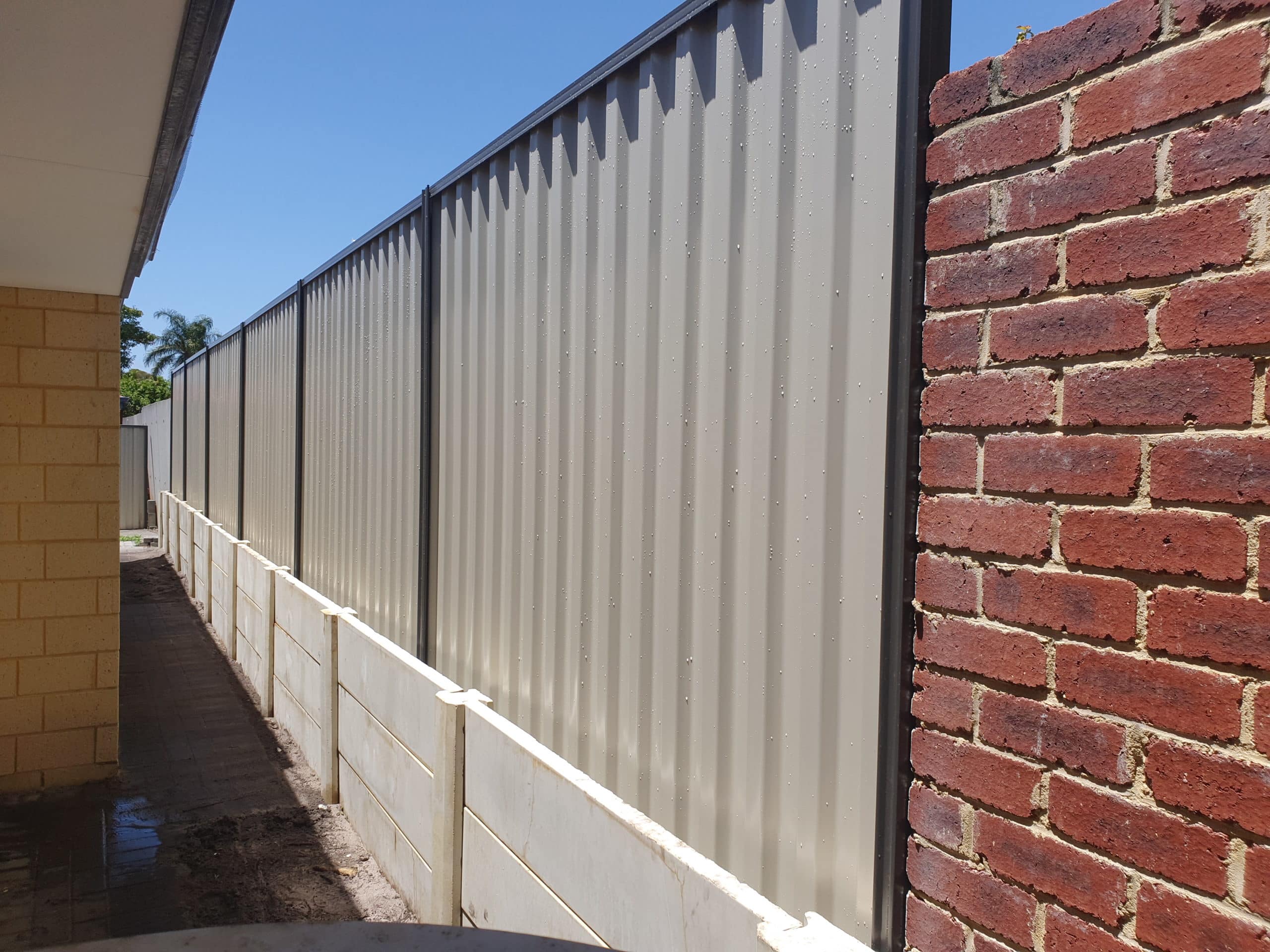 Colorbond fence installation on a retaining wall in Perth, providing a practical and attractive solution for defining property boundaries and retaining soil. The Colorbond fence panels are installed on top of a sturdy retaining wall, creating a solid barrier for privacy and security. The fence comes in a range of colors to match the surrounding landscape or house exterior and is known for its durability and low maintenance. The fence installation team can customize the design and height of the fence to meet the specific needs and preferences of the property owner, ensuring a functional and stylish addition to the property