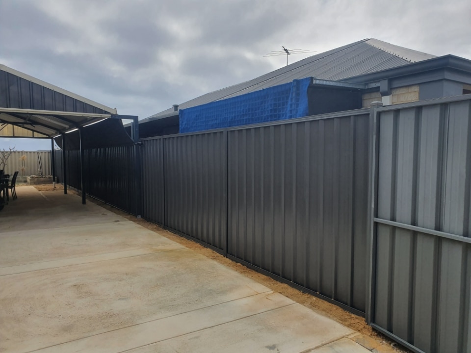 A Colorbond fence and gate installed in Perth, featuring a sleek and modern design with clean lines and a smooth finish. The fence panels are made of durable Colorbond steel, which comes in a range of colors to match the surrounding landscape or house exterior. The matching gate provides easy access while maintaining the same aesthetic appeal and security as the fence.